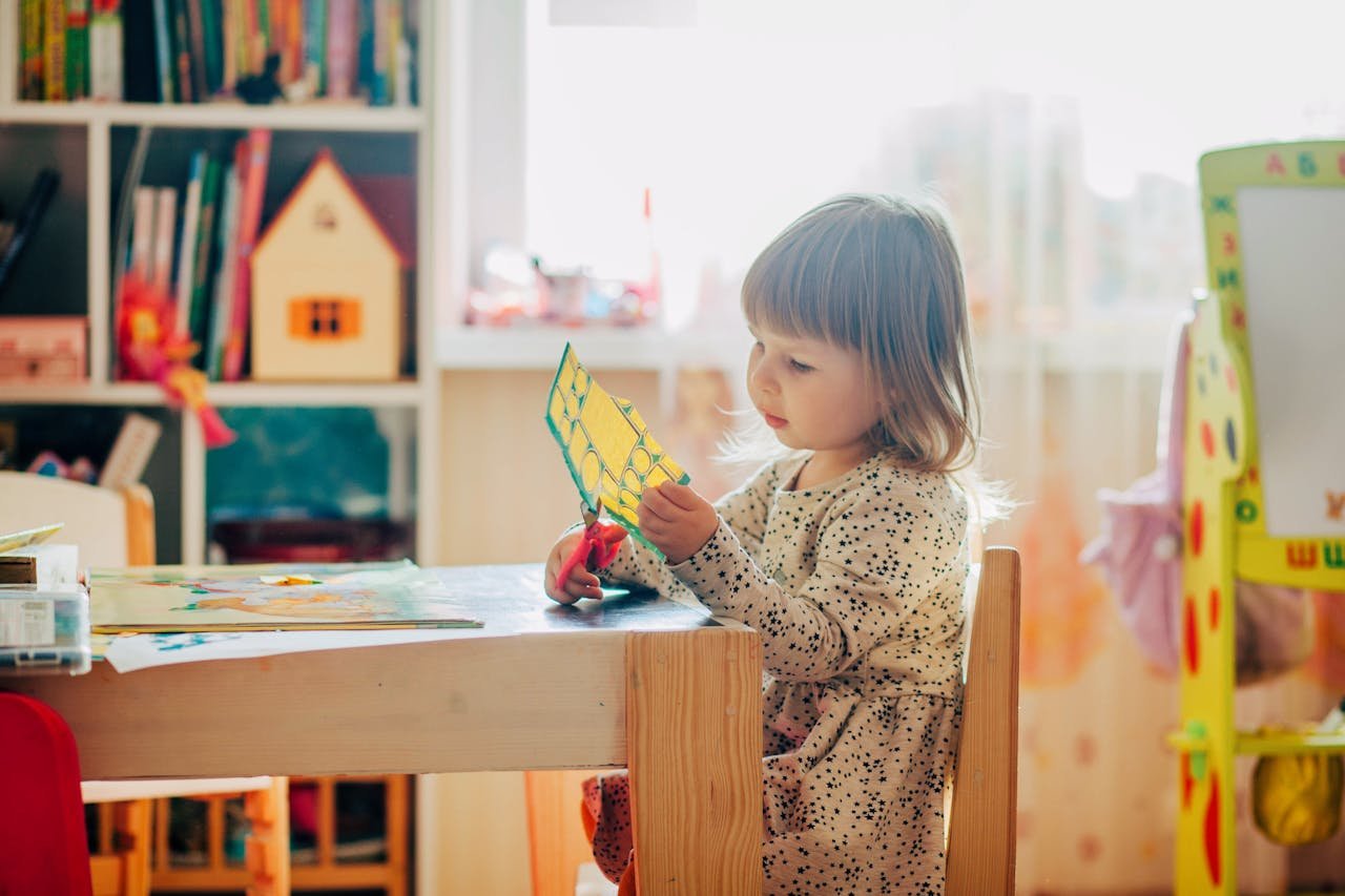 Young girl concentrating on arts and crafts using colorful paper and scissors indoors.